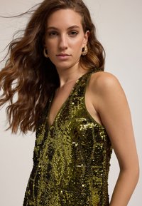 Rochie verde din paiete cu decolteu în V, având un model geometric, accente metalice și o siluetă ajustată.