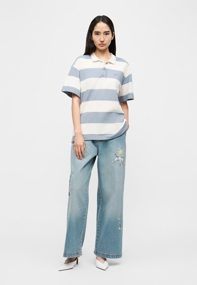 Ριγέ πόλο πουκάμισο σε ανοιχτό μπλε και λευκό, με γιακά και κουμπιά, σε συνδυασμό με τζιν παντελόνι φαρδιάς γραμμής με φθορές και διακοσμητικά στοιχεία.