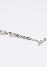 Pulsera de metal plateado con eslabones en forma de corazón y un cierre en forma de corazón, con una textura suave y brillante y un diseño contemporáneo.