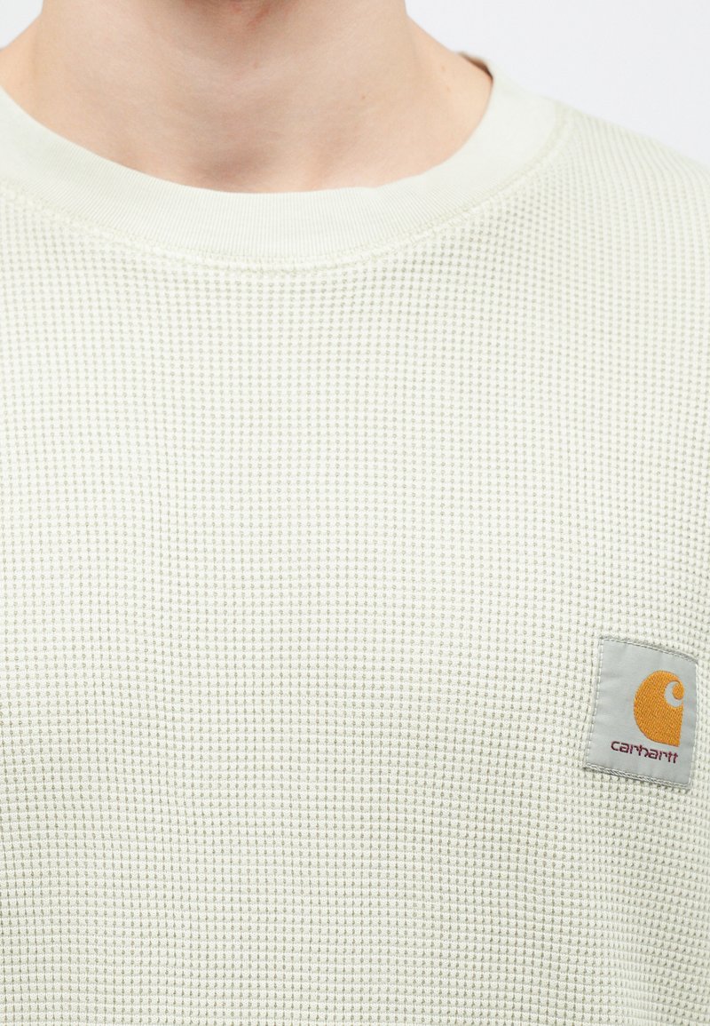 Lysegrøn waffle-strikket sweatshirt med en ribbet hals, prydet med et firkantet logo NFL med en orange accent.