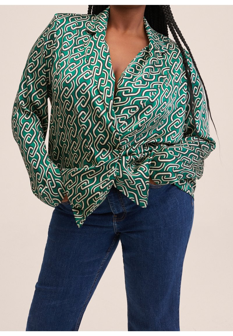 Grüne Bluse mit Muster und Knoten-Design, die ein geometrisches Kettenmuster in Weiß und Beige aufweist, aus glattem Stoff gefertigt.