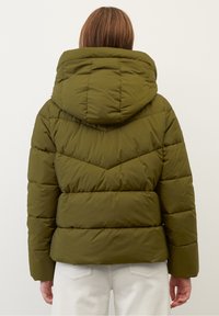 Olivgrön vadderad jacka med huva, med ett quiltat mönster och sicksackdesign. Materialet verkar mjukt och isolerat.