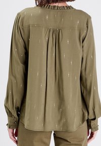 Blouse vert olive en tissu doux, avec un col à volants, des manches longues et de délicates accents métalliques en lignes verticales.