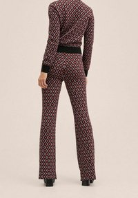 Conjunto de dos piezas en patrón rojo y negro con chaqueta ajustada y pantalones acampanados. Presenta mangas largas y puños acanalados. Textura de tela suave.