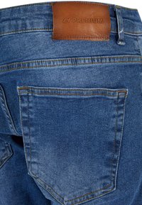 Jean en denim avec une teinte bleu clair, arborant une étiquette en cuir marron portant la mention "2Y PREMIUM" et des coutures visibles sur les poches arrière.