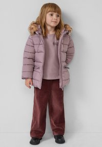 Lichtpaarse, puffy jas met een faux-fur rand bij de capuchon, gedragen over een bijpassend topje, in combinatie met rode corduroy wijduit broek en zwarte laarzen.