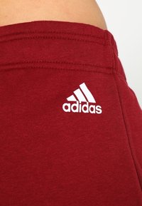 Pantalones de chándal rojos de algodón con un logo blanco de Adidas en el muslo, con una textura suave y una cintura elástica.