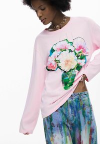 Hele heleroosa pusaga, millel on lillemuster roosa, valge ja rohelise toonides. Ühildatud siniste, plekipritsmetega teksadega.