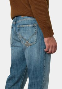Jeans in denim azzurro chiaro con vestibilità dritta, abbinati a un maglione a coste marrone testurizzato e un design con tasche triangolari.