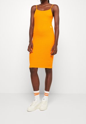 Pomarańczowa, dopasowana sukienka midi bez rękawów z cienkimi ramiączkami, zestawiona z białymi trampkami oraz białymi skarpetkami z pomarańczowymi paskami.