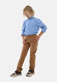 Chemise bleu clair à boutons avec une poche poitrine, associée à un pantalon en velours côtelé marron et des baskets multicolores ornées de lacets et de détails.