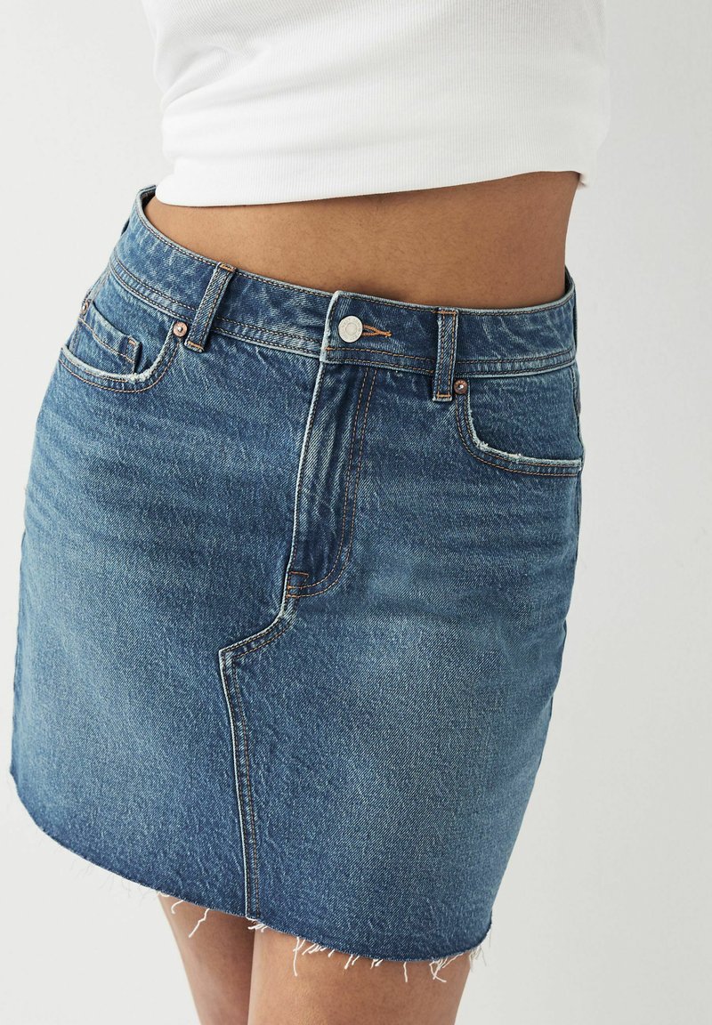 Denim minikjol med fransat fåll, ljusblå tvätt, femfickorsdesign och kopparfärgad hårdvara. Klassisk passform, avslappnad stil.