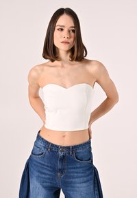 Top corto bianco senza spalline con scollatura a cuore, abbinato a jeans blu a vita alta con vestibilità rilassata e tasche frontali.
