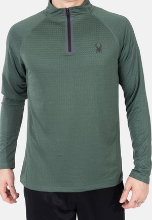 Pull-over léger à manches longues vert avec un zip 1/2 à l'avant, en tissu texturé, et un logo noir sur la poitrine. Ajustement élastique, coupe athlétique.