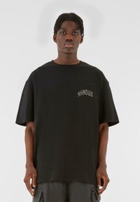 Sort oversized t-shirt lavet af bomuld, med rund halsudskæring og korte ærmer, med "MJ GONZALES" trykt i lysegrå på brystet.
