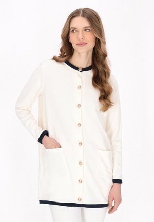 White cardigan with navy accents, button closure, and two front pockets. Features a soft texture and a round collar.