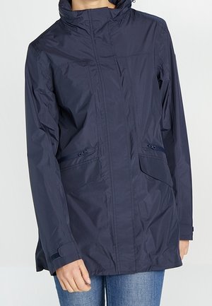 Veste légère bleu marine avec col montant, fermeture éclair à l'avant, poches zippées et à rabat, portée par une personne en jean.