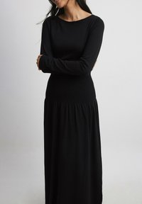 Black long-sleeve dress with a fitted top and flared, gathered skirt. Made from soft material, featuring a rounded neckline and minimal design.