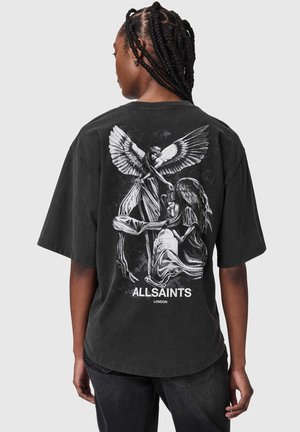 Person mit geflochtenem Haar trägt ein schwarzes T-Shirt mit weißen engelsgleichen Figuren und dem Text „ALLSAINTS LONDON“ auf dem Rücken.
