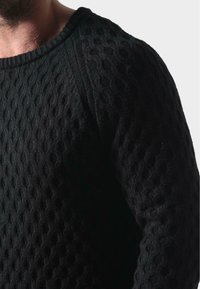 Czarny sweter z dzianiny z teksturowanym wzorem, okrągłym dekoltem oraz prążkowanymi detalami przy mankietach i obrzeżu.