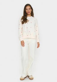 Ljuscremefärgad sweatshirt med spridda röda hjärtan, ribbade muddar och nederkant. Matchas med vita vida byxor och beige sneakers.