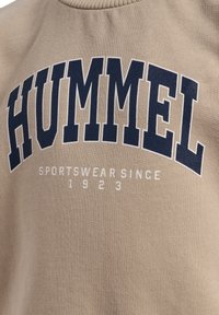 Beiger Sweatshirt mit "HUMMEL"-Logo in Marineblau, mit lockerer Passform, geripptem Kragen und strukturiertem Material. "SPORTSWEAR SINCE 1923" in Weiß.
