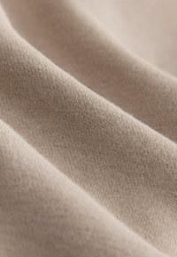 Tissu beige clair avec une texture lisse, présentant de fins motifs de tricot et une légère douceur, drapant en douces vagues.