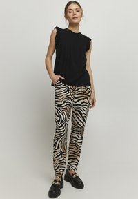 Zwarte mouwloze top met gerimpelde rand; gecombineerd met beige en zwart gestreepte broek met zebra-patroon; model draagt chunky zwarte instappers.