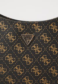 Fekete szintetikus kézitáska, arany logo mintával és fém háromszög alakú logolemezzel, amelyen a "GUESS USA" felirat olvasható.