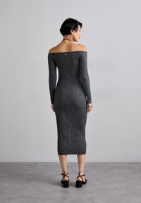 Šaty s odhalenými rameny, obepnutého střihu vyrobené z šedého ribbového materiálu. Elegantní dlouhé rukávy, délka po lýtka, s detailem švu na zadní straně. Stylizováno s robustními černými podpatky.