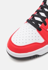 Baskets rouges et blanches avec une tige en cuir blanc perforé, des accents en cuir rouge, des lacets noirs et une semelle en caoutchouc noire.