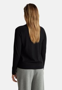 Czarny sweter z okrągłym dekoltem, ribbowanym dołem i długimi rękawami, w połączeniu z szarymi spodniami dresowymi. Gładka tekstura z minimalnymi detalami.