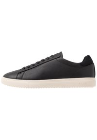 Black sneaker with a smooth leather upper, round toe, minimalistic design, and a white rubber sole with textured tread for grip.