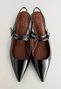 Mustat kiiltonahkaiset slingback-kengät, joissa on terävät kärjet, kaksi ristikkäin olevaa hihnaa ja hopeinen solk yksityiskohta. Ruskeat sisäpohjat, joissa lukee "NEXT Forever Comfort."