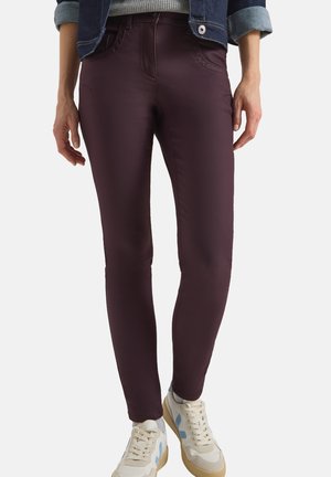 Burgundské skinny džíny s hladkým povrchem, vybavené předními kapsami a standardním pasem, spárované s bílými a béžovými teniskami.