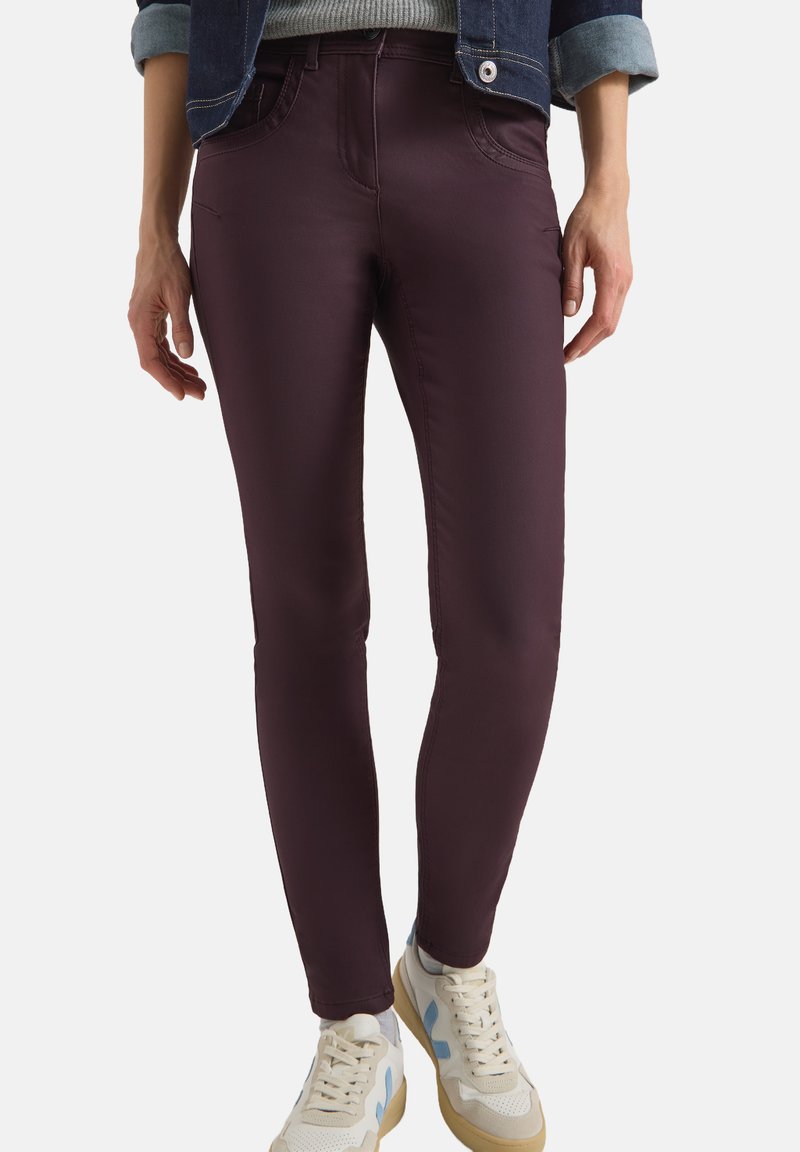 Bordeaux skinny jeans met een gladde textuur, voorzien van achterzakken en een standaard tailleband, gecombineerd met witte en beige sneakers.