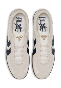 Adidași texturați alba cu dungi bleumarin, având un design cu șireturi și un logo în formă de fagure de miere în aur pe limba pantofului. Talpă din cauciuc.