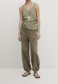 Olive green, ribbed tank top paired with loose, suede-like olive trousers. Features a long pendant necklace and strappy black sandals.
