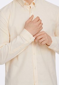 Camicia button-up giallo chiaro con una sottile trama, maniche lunghe e polsini con bottoni, caratterizzata da un design colletto classico.