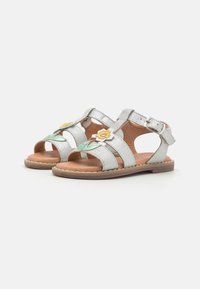 Silberne Glitzersandalen mit drei Riemen, floralen Akzenten in Gelb und Grün, verstellbarem Schnallenverschluss und brauner Sohle. Texturiertes Innenfutter.
