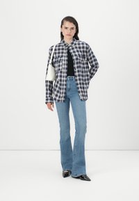 Camisa de botão xadrez em azul-marinho e branco, topo preto, jeans flare de cintura alta em azul claro, e sapatos pretos brilhantes de bico fino. Bolsa branca.