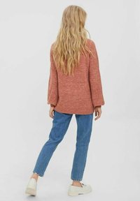 Svetr rustové barvy s texturovaným úpletem a dlouhými rukávy, v kombinaci s rovnými modrými džínami a světlou obuví. Neformální, pohodlný střih.