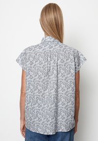 Lyhythihainen paita vaaleanharmaasta kankaasta, jossa on kukkakuosi. Selän laskos ja pieni kaulus korostavat mallia.