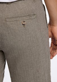 Pantalons en chevrons marron clair avec une poche arrière à bouton. Le tissu a un tissage texturé et une coupe ajustée.