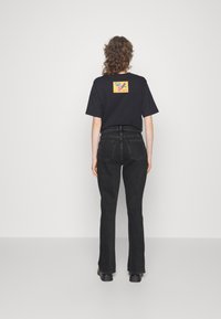 Black cotton t-shirt with a colorful flower design patch on the back, paired with high-waisted black jeans and chunky black footwear.