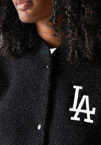 Schwarze Fleecejacke mit strukturierter Oberfläche, ausgestattet mit einem gerippte Kragen und einem weißen "LA"-Logo auf der oberen linken Seite.