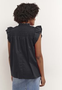 Camiseta neagră cu mâneci scurte și umeri volănați, având un spate plisat și un guler înalt. Material fin, ușor.