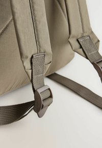 Rucsac khaki cu țesătură texturată, curea laterală de prindere și cusături întărite. Bretelele sunt ajustabile și au un design țesut.