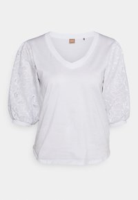 Bílý V-krkový tričko s krátkými, nabíranými rukávy, zdobené květinovou krajkou. Měkký materiál, volný střih, s vroubkovaným výstřihem a manžetami.