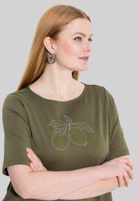 Olivově zelená košile s krátkým rukávem s designem citronů pokrytých žlutými a bílými tečkami. Hladký materiál, kulatý výstřih a volný střih.